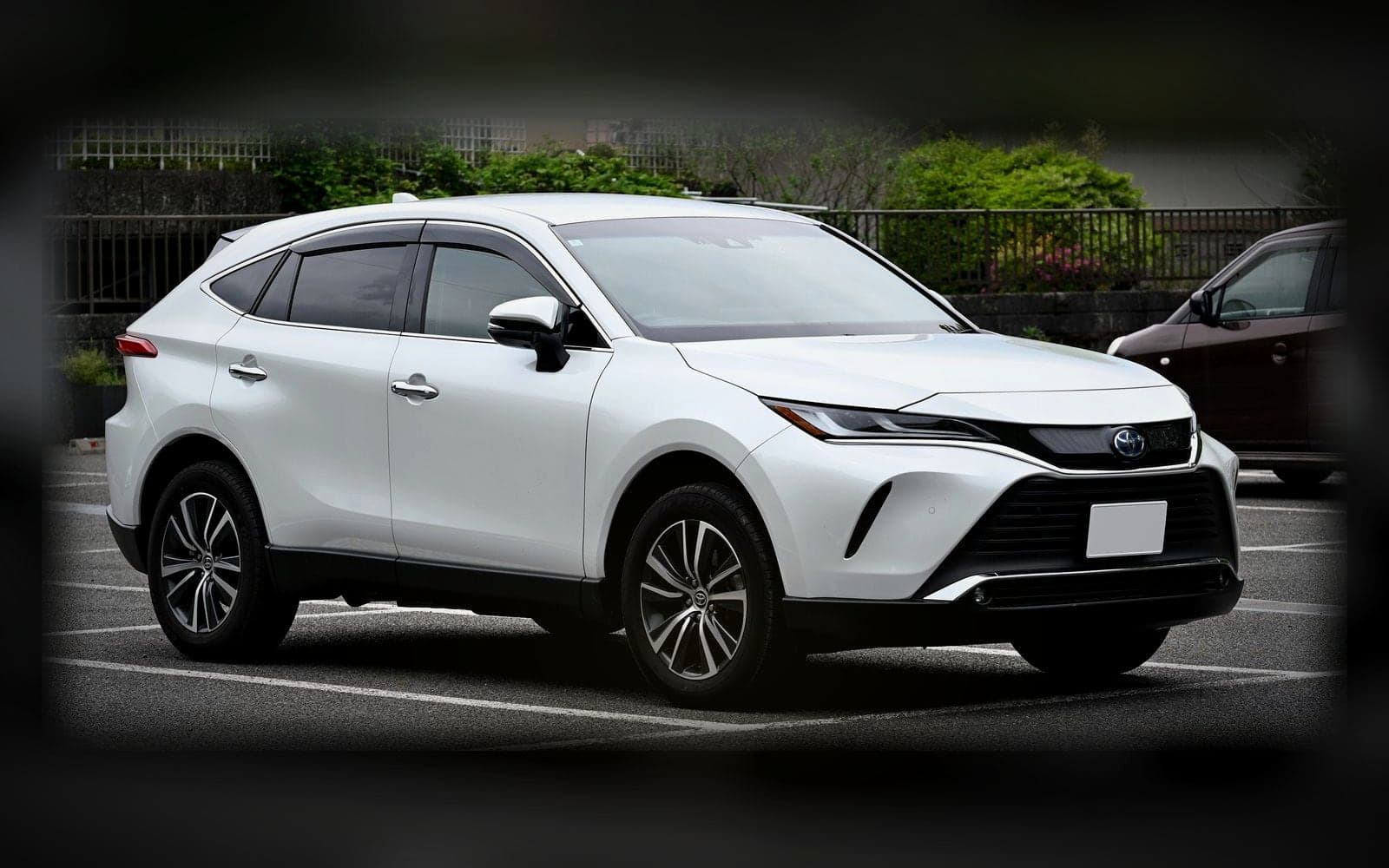 A white Toyota Harrier, the executive 4x4 class, lit against a dark showroom backdrop