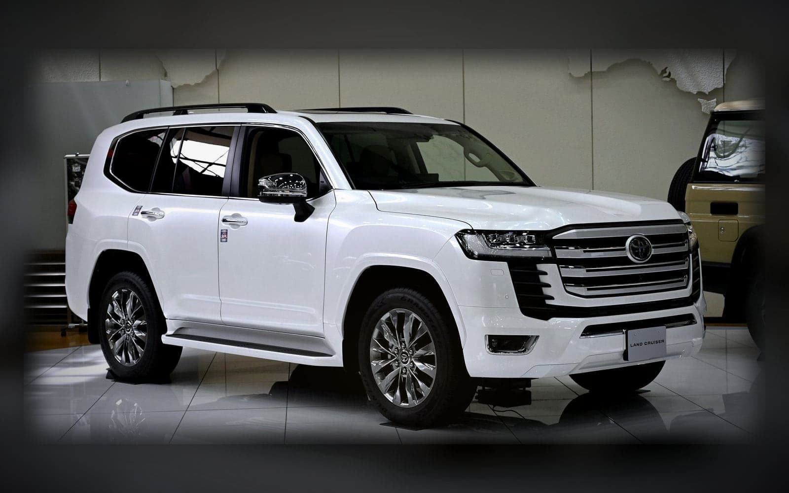 A white Toyota Land Cruiser 300, the flagship 4x4 class, lit against a dark showroom backdrop