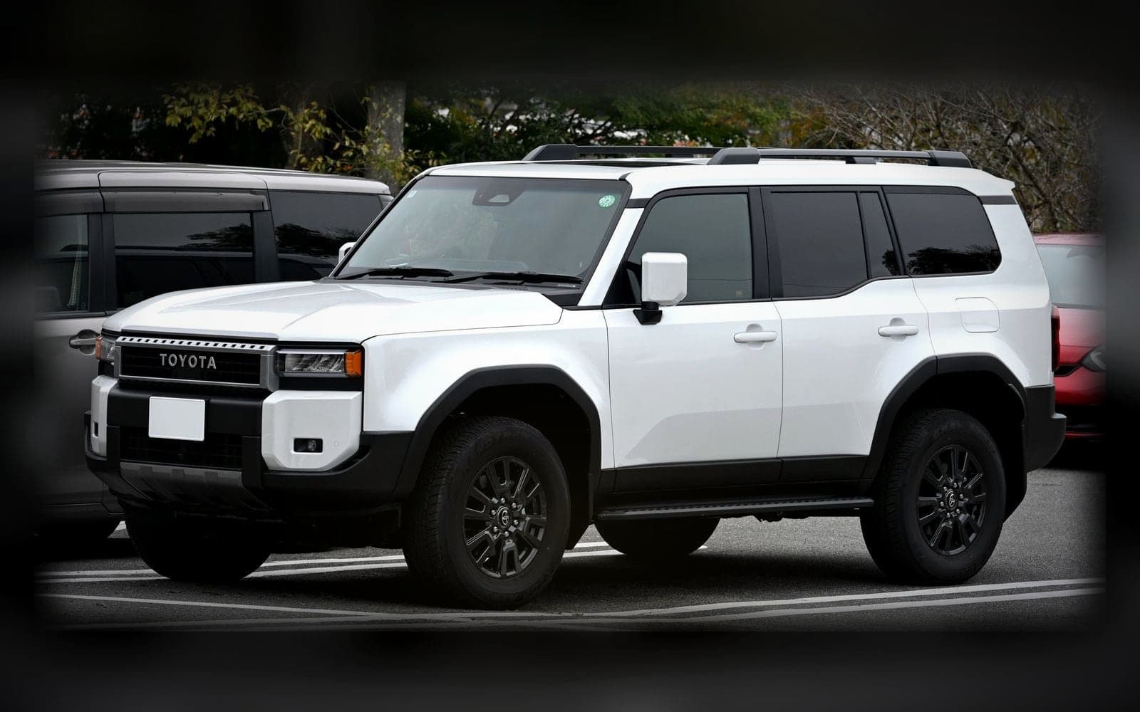 A white Toyota Land Cruiser Prado, the luxury 4x4 class, lit against a dark showroom backdrop